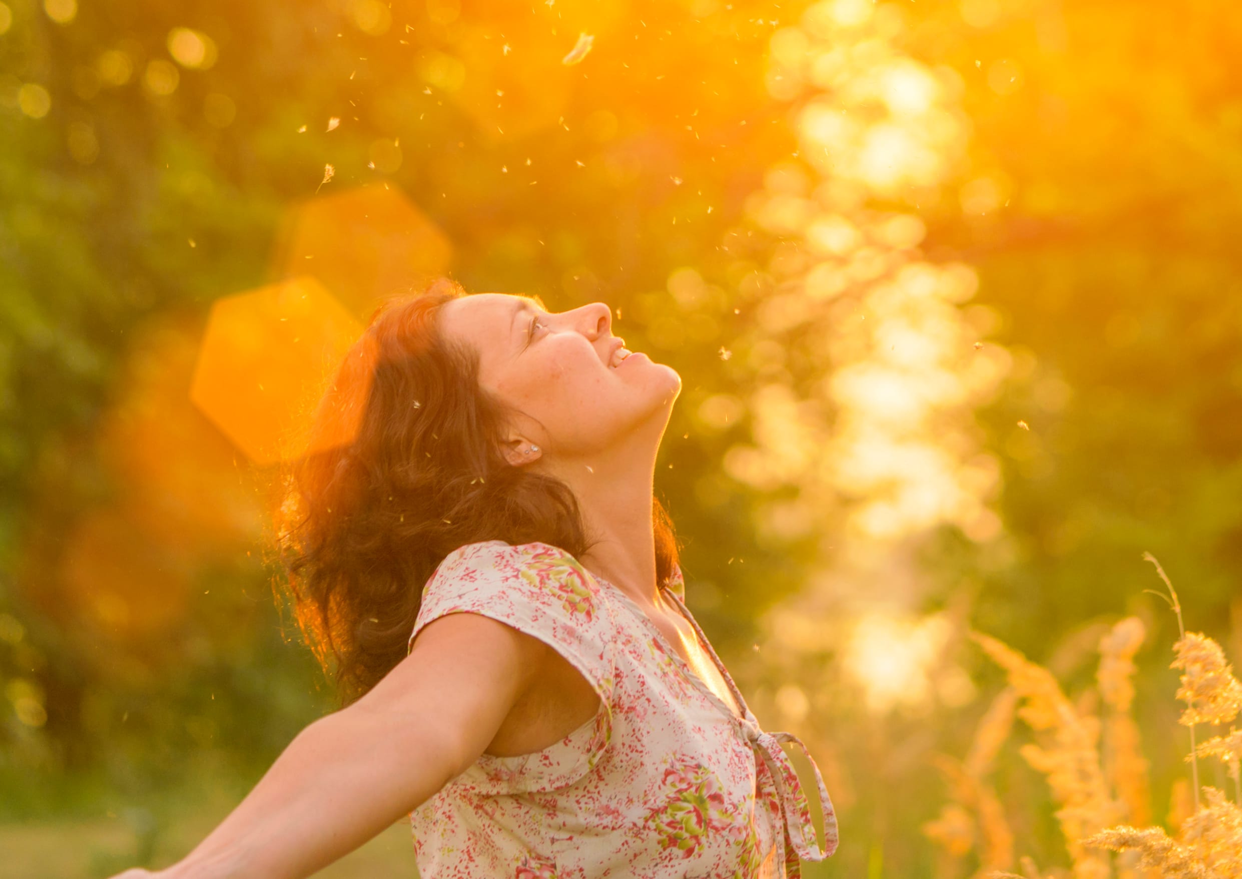 woman in a dress throws up grass in a meadow near the trees in the sunlight